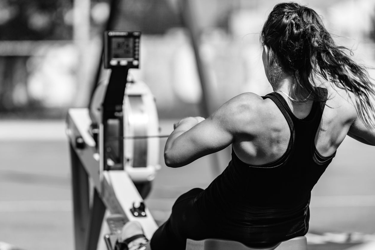 Black and white photo of a woman using a rowing machine in a gym.