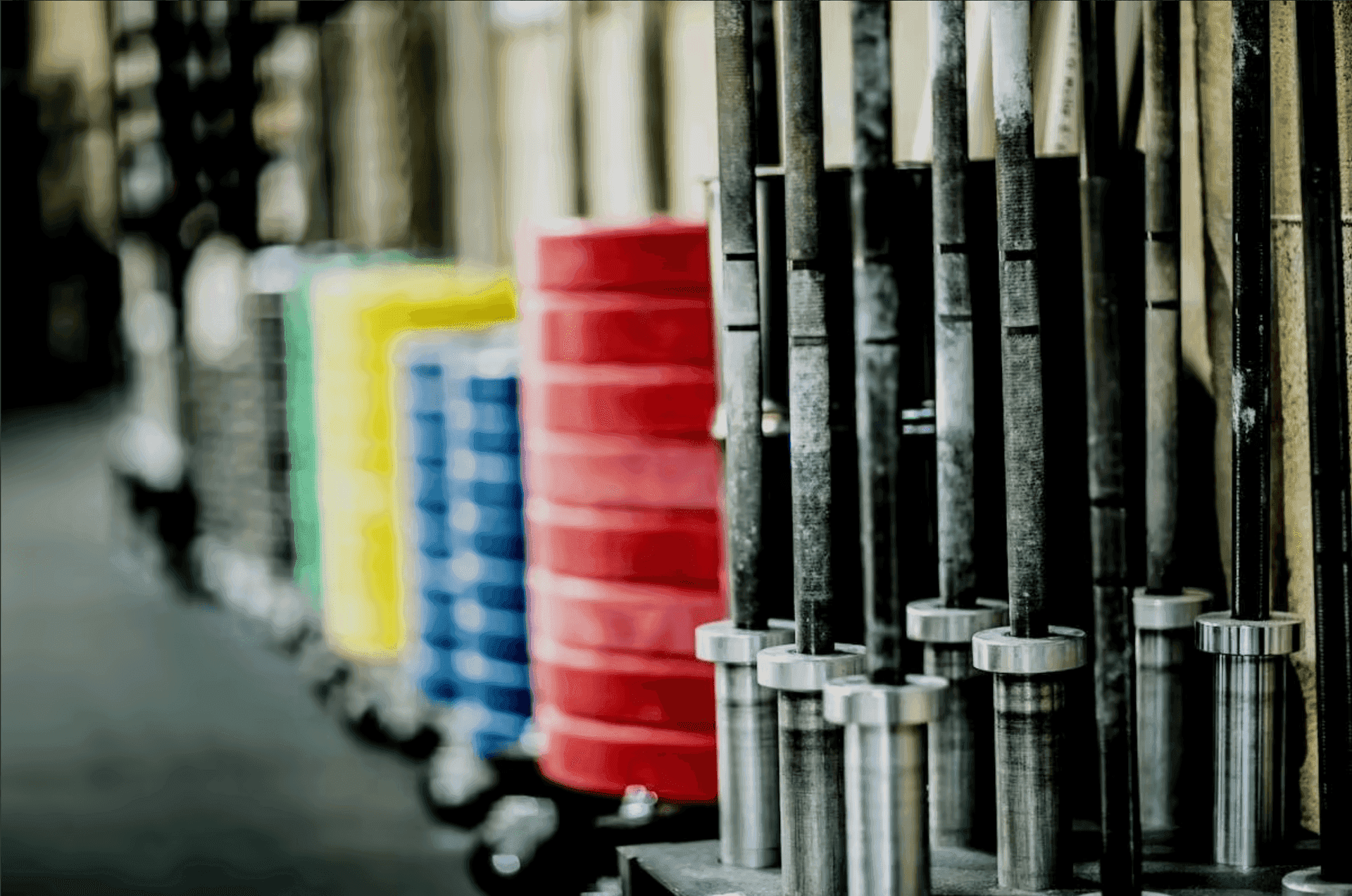 Colorful weightlifting plates stacked on racks with a row of barbells in focus.